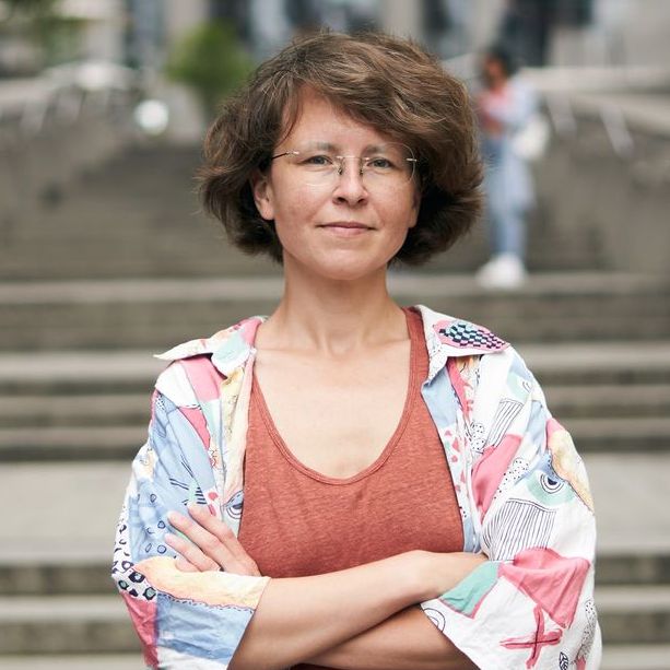 Woman with short brown hair and rimless eyeglasses standing outside in front of a grand concrete staircase.