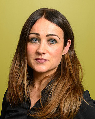 A headshot of a woman with brown, mid-length hair standing in front of a green backdrop.